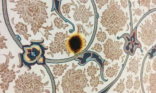 Ein orientaler Teppich mit floralen Mustern und einer verbrannten Stelle in der Mitte.