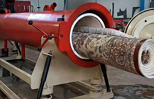 Eine Maschine zur Teppichreinigung, die einen aufgerollten, gemusterten Teppich teilweise in einer rot lackierten Trommel hält.