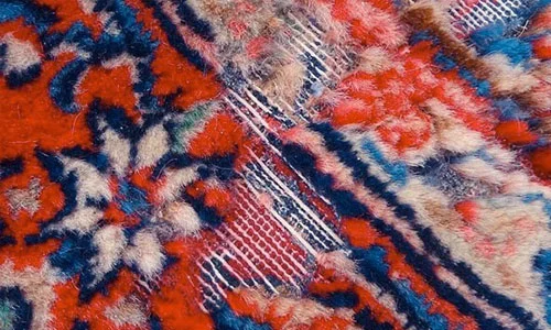 Nahaufnahme eines gewebten Orientteppichs mit roten, blauen und weißen Mustern und sichtbarem Verschleiß an einigen Stellen.