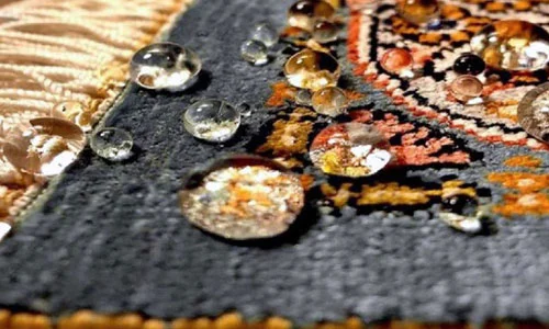 Nahaufnahme eines gewebten Teppichs mit detaillierten Mustern in Blau und Orange, auf dem mehrere klare Wassertropfen liegen.
