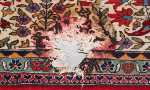 Nahaufnahme eines orientalischen Teppichs mit einem großen Loch in der Mitte, umgeben von floralen und geometrischen Mustern in Rot-, Blau- und Beigetönen.